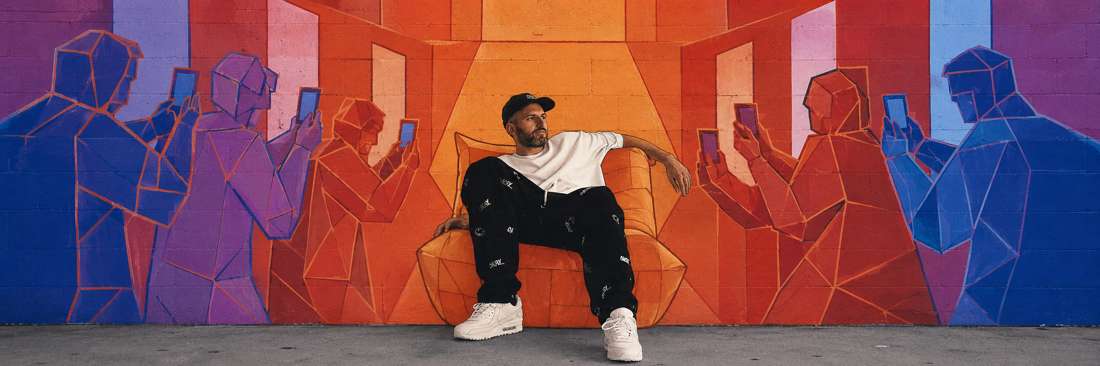 Harry Mack seated in front of a vivid mural, framed by an audience holding up phones.